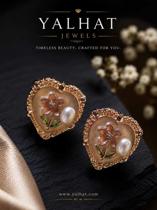 Heart-shaped earrings with floral design and pearl accents on a dark surface, branded as Yalhat Jewels.
